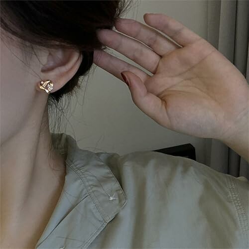 Kvinna håller handen vid örat med guldörhänge
